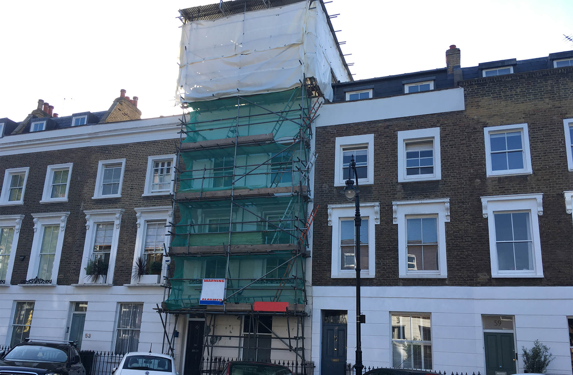 scaffolding tower on a terraced house with green netting and roof cover